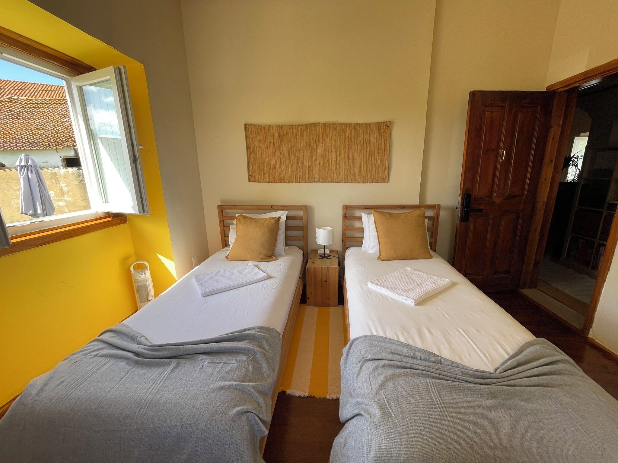A room with two beds, a window, a door, and a wall-mounted artwork.