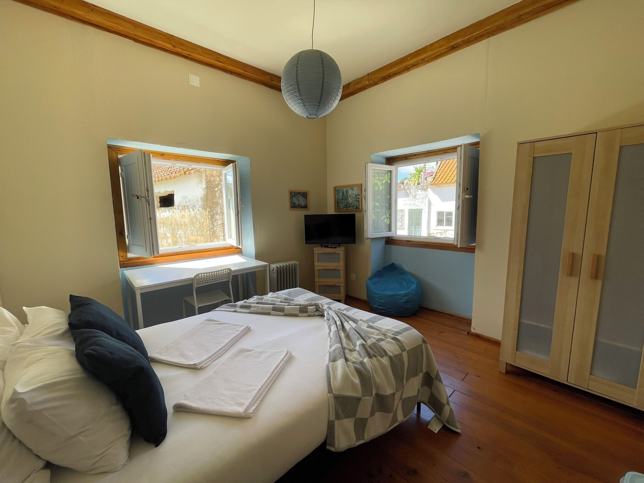 A bedroom with a bed, two windows, a television, a radiator, and a wardrobe.