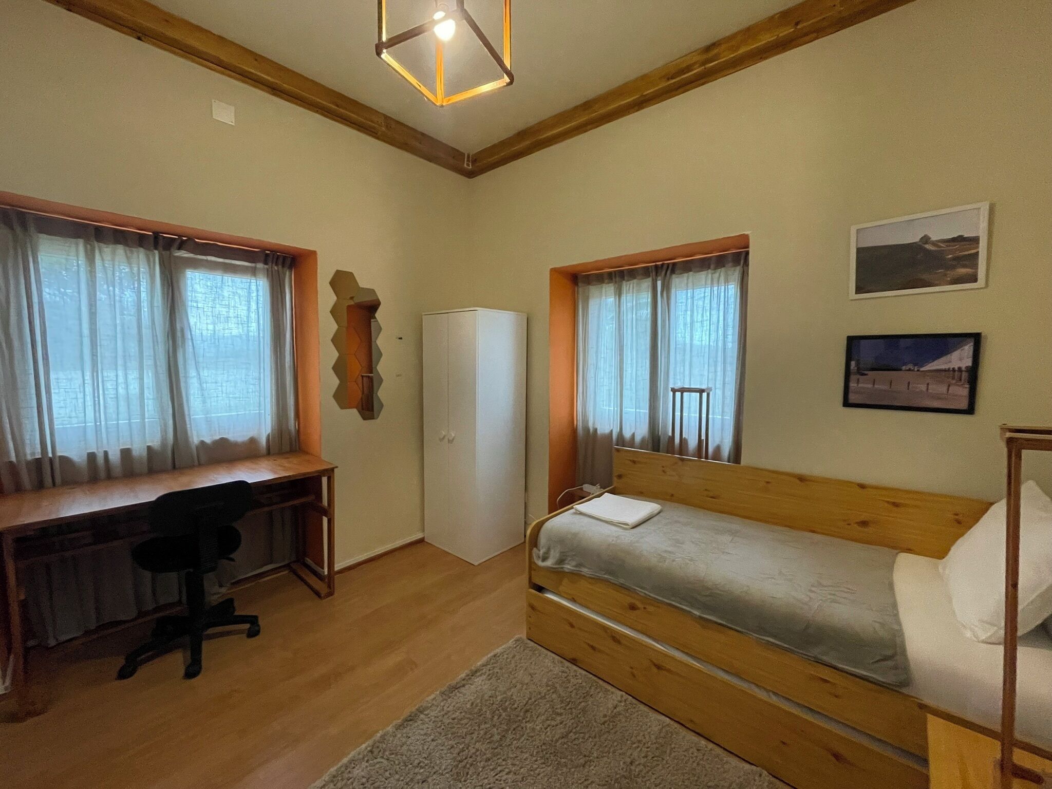 A bedroom with a wooden bed, a desk with a chair, a wardrobe, and a small table.