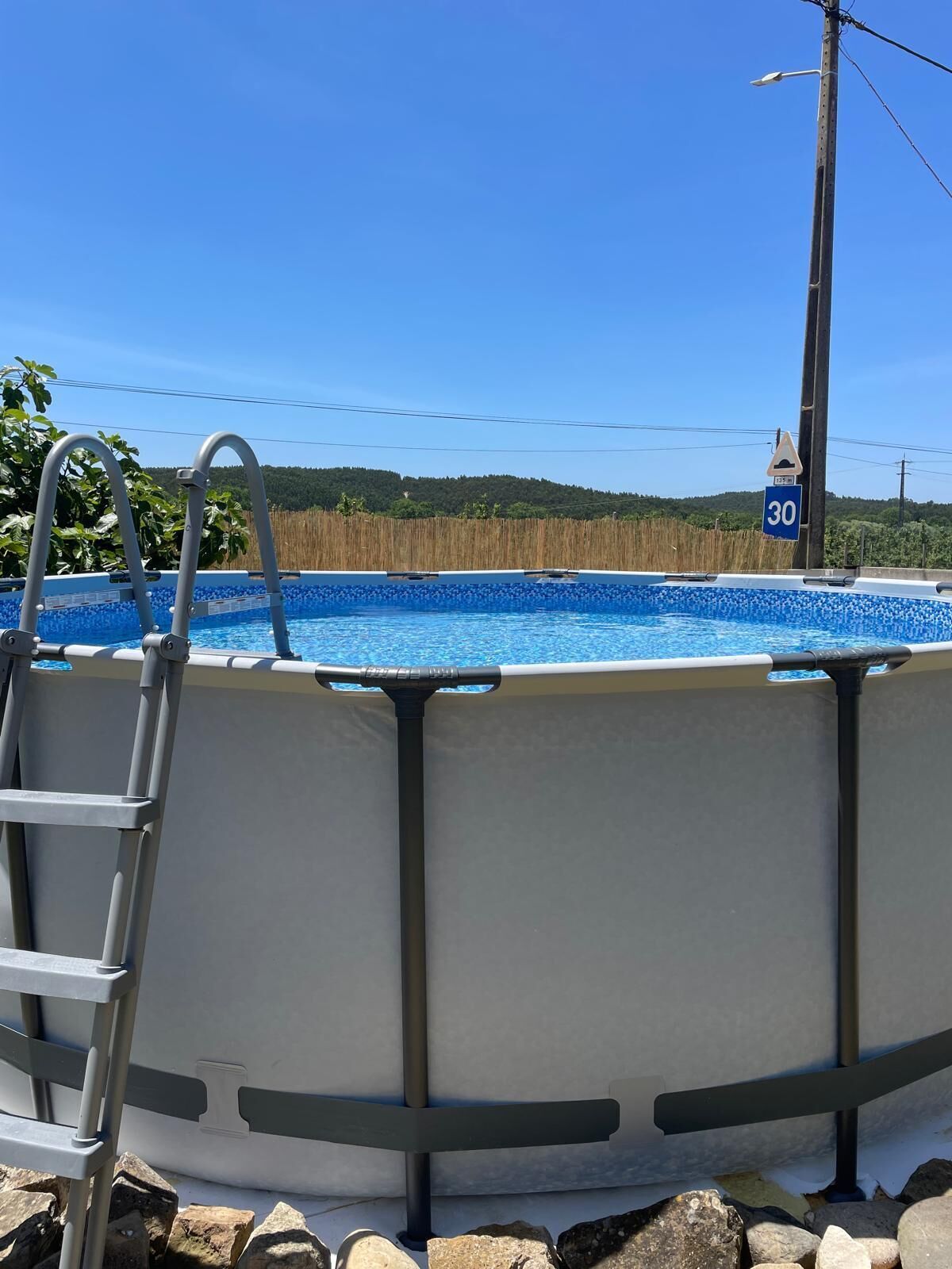 Una piscina circular con una escalera, rodeada de rocas, y una señal de límite de velocidad al fondo.