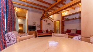 A cozy room with a round wooden table, two sofas, a TV, and a bed with red bedding. - Principe Marmolada 817/A (Rocca Pietore)