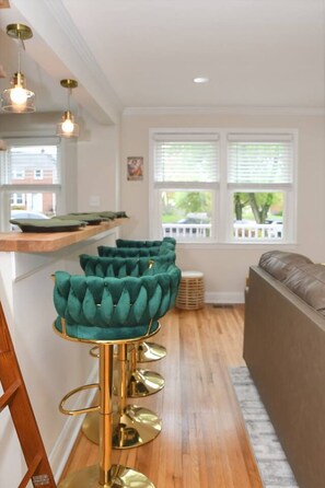 A modern kitchen with a bar area featuring green upholstered bar stools with gold accents and a brown leather sofa. - Jazzkey Suite & Kindred Retreat (Parkville)