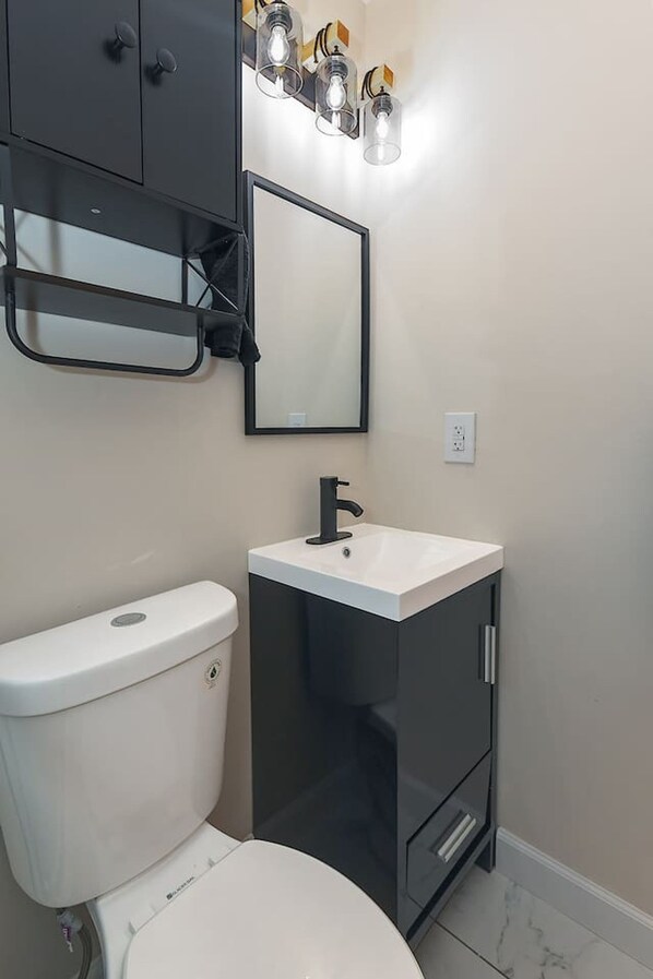 A bathroom with a toilet, a sink, a mirror, and a cabinet. - Jazzkey Suite & Kindred Retreat (Parkville)