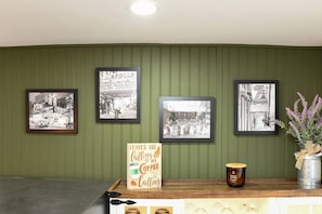 Un mur orné de photographies en noir et blanc encadrées, une enseigne sur le café et un seau en métal rempli de fleurs.