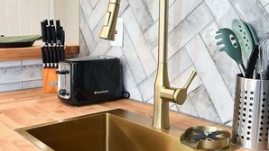 Uma cozinha com uma torneira dourada, uma torradeira e um suporte para facas sobre o balcão.