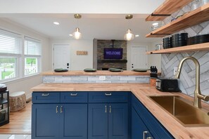 A modern kitchen with blue cabinets, wooden countertops, a built-in stove, and a welcoming sign.