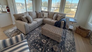 A living room with a sectional sofa, a patterned rug, and large windows offering a view of the neighborhood. - “The Delford” Beach House only Steps to the Bay Beaches (Lower Township)