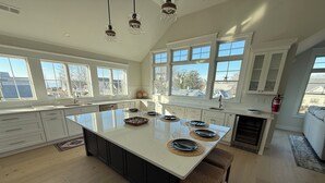 A spacious kitchen with a large island, white cabinetry, and large windows offering views of the neighborhood. - “The Delford” Beach House only Steps to the Bay Beaches (Lower Township)