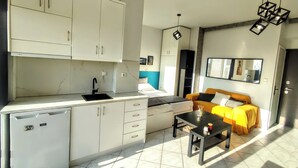 Un espacio habitable compacto con kitchenette, una cama con colcha amarillo y negro, una mesa de comedor y una lámpara colgante moderna.