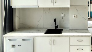 Una cocina compacta con armarios blancos, un lavamanos empotrado y un refrigerador pequeño.