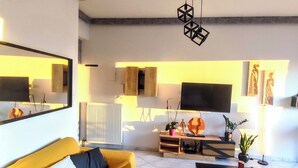 Una sala de estar moderna con un sofá amarillo, una mesa de centro negra y un televisor de pantalla plana montado en la pared.