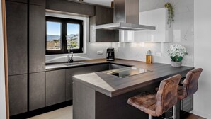 A modern kitchen with a large island, dark cabinetry, and a window offering a view of the outdoors.