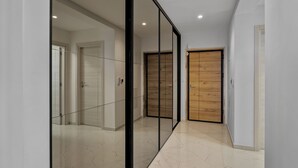 A hallway with glass doors, a wooden door, and a tiled floor.