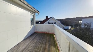 A balcony with a wooden floor, white walls, and a clear view of a house in the background. - Two Apartments in Central Skärhamn | SE09100 (Skärhamn)