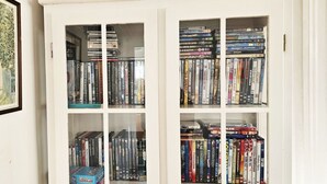 A bookshelf filled with DVDs and books, a framed picture of a dog, and a window with a view of a building. - Two Apartments in Central Skärhamn | SE09100 (Skärhamn)