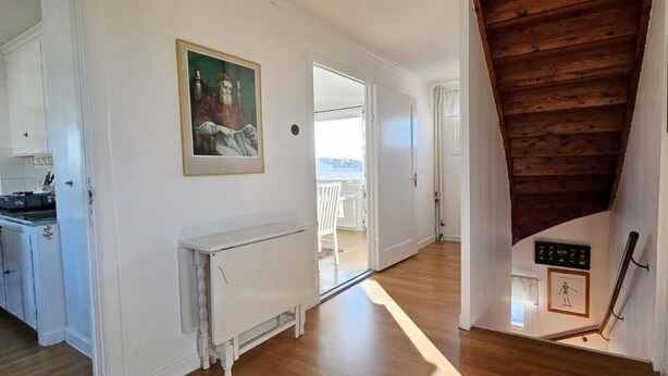 A hallway with a wooden staircase, a radiator, and a framed picture on the wall. - Two Apartments in Central Skärhamn | SE09100 (Skärhamn)