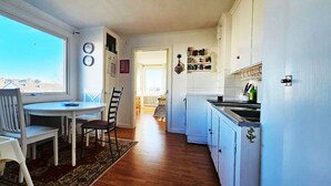 A kitchen with white cabinets, a dining table with chairs, and a view through a window. - Two Apartments in Central Skärhamn | SE09100 (Skärhamn)