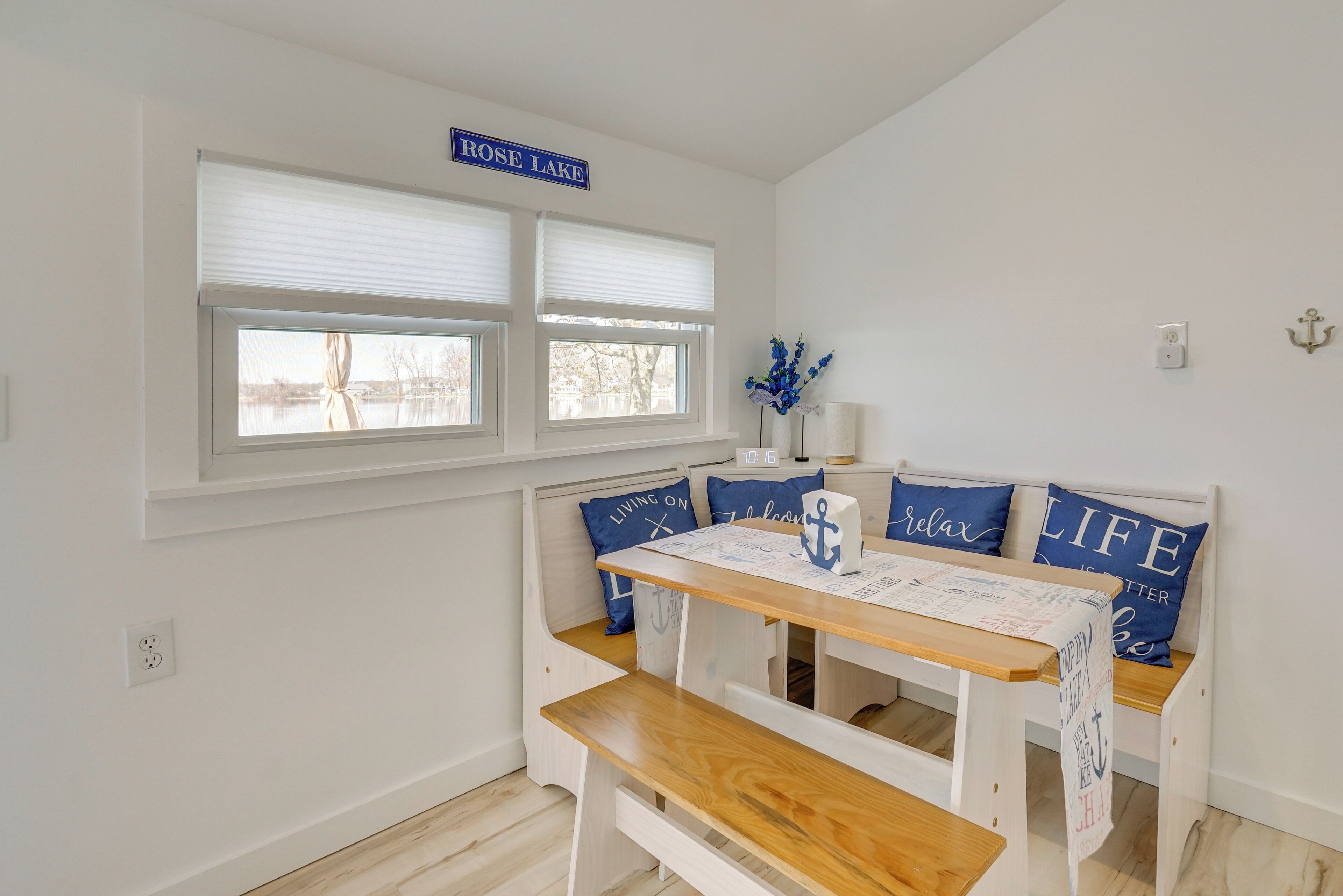 A room with a bench seating area, a table with a placemat, and a window with a sign reading "ROSE LAKE".