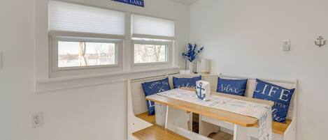 A room with a bench seating area, a table with a placemat, and a window with a sign reading "ROSE LAKE".