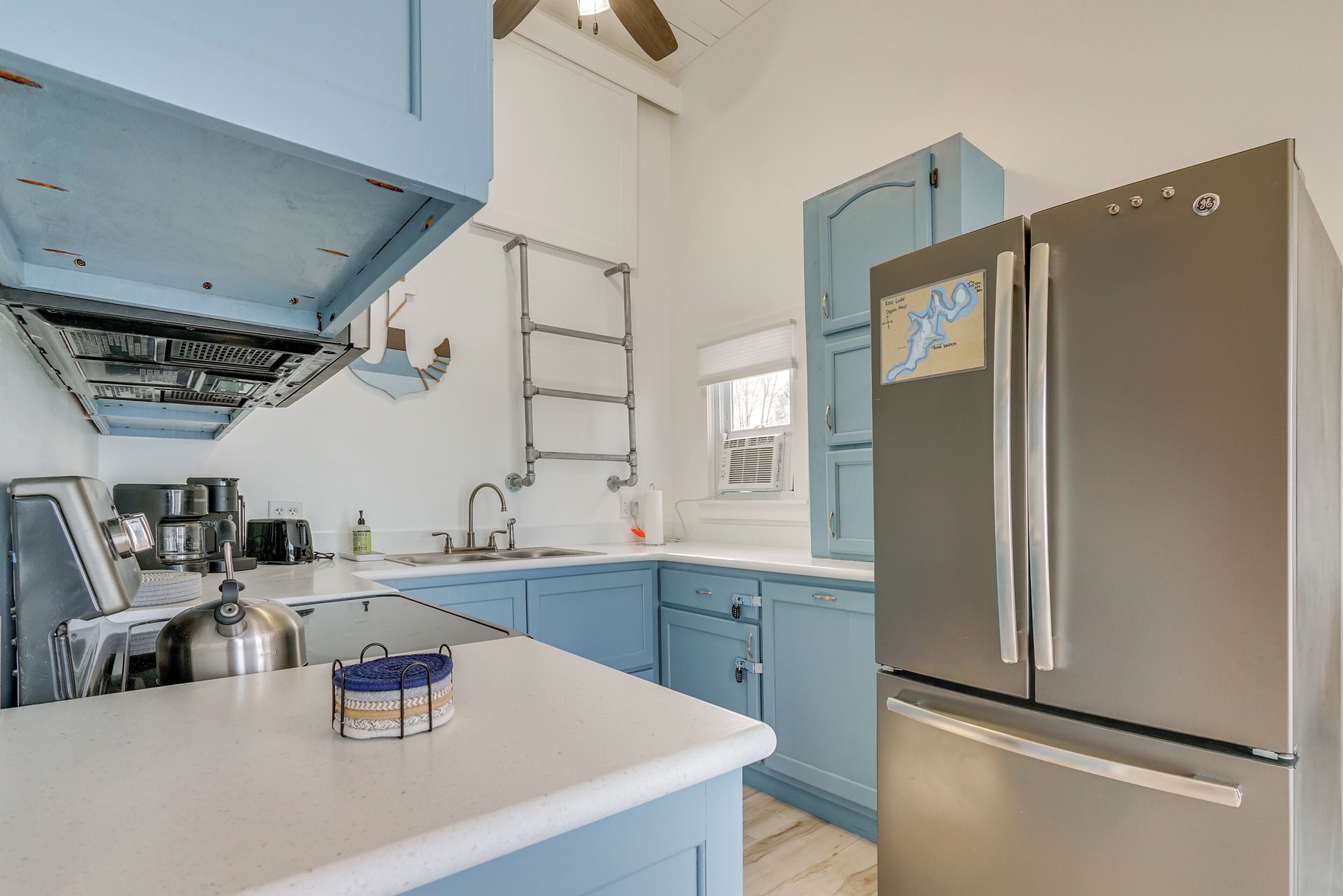 A kitchen with blue cabinets, a stainless steel refrigerator, and a kettle on the counter.