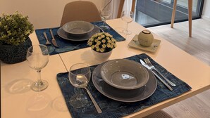 A dining area with a table set for two, a clock on the wall, and a window with blinds.
