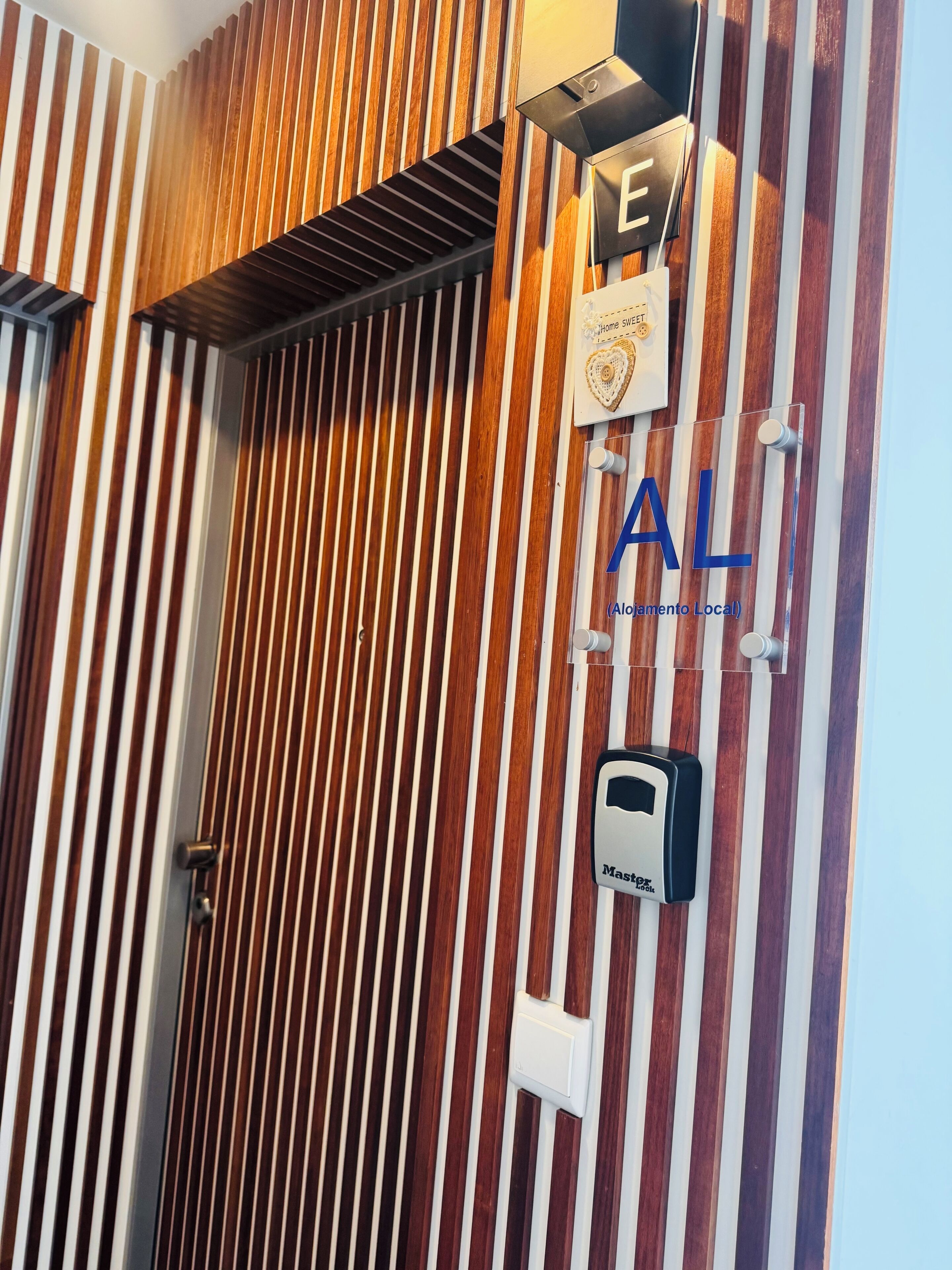 A wall with vertical wooden slats and a sign with the letters 'AL' and 'Alojamiento Local'.