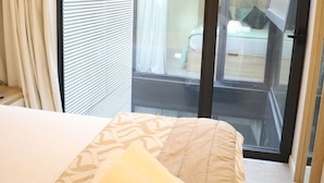 A hotel room with a bed, a window with blinds, and a view of the outside balcony.