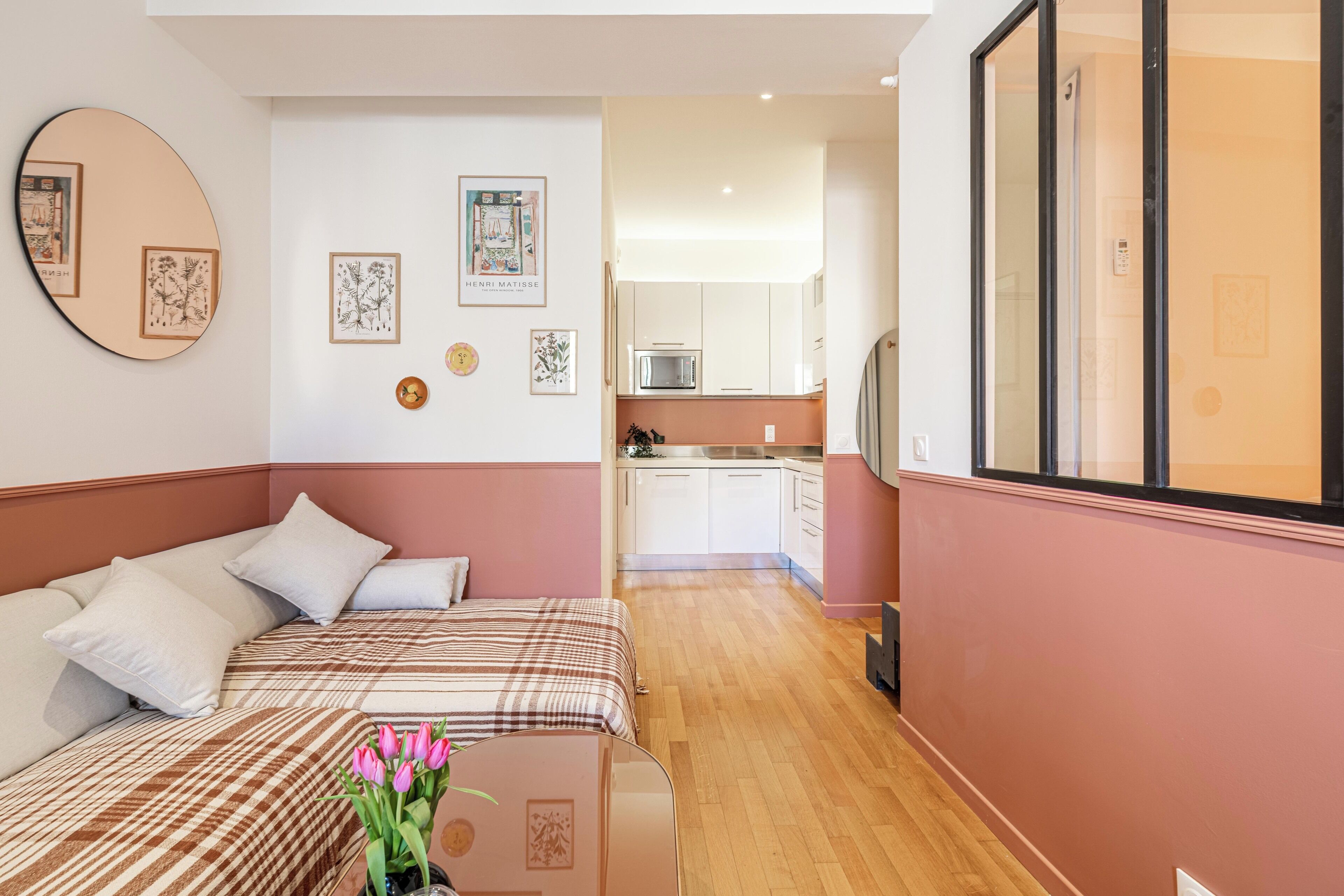 Un dormitorio con dos camas, una mesita con un jarrón de flores y una cocina al fondo.
