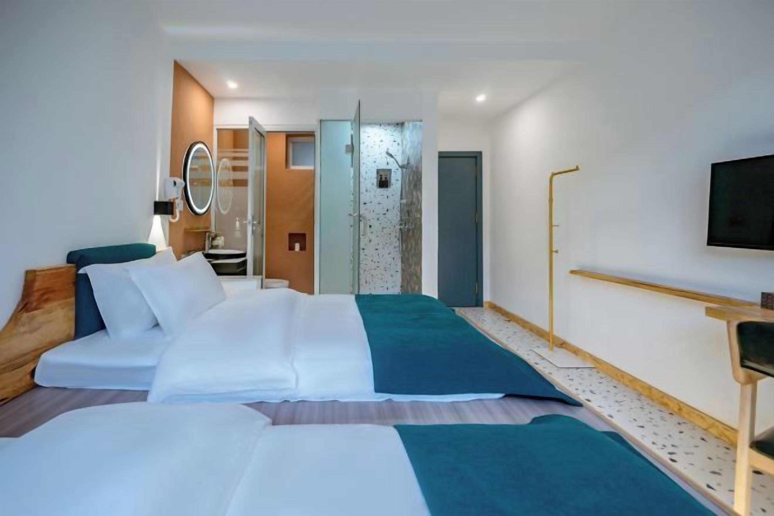 Une chambre d’hôtel moderne équipée d’un lit, d’une télévision, d’un miroir et d’une salle de bain visible à travers une porte ouverte.