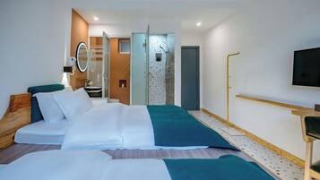 Une chambre d’hôtel moderne équipée d’un lit, d’une télévision, d’un miroir et d’une salle de bain visible à travers une porte ouverte.