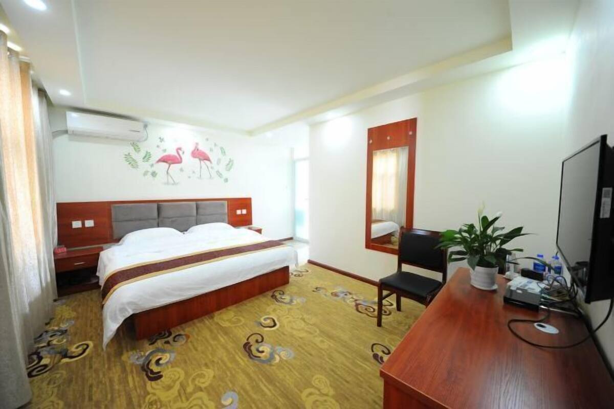 A hotel room with a bed, a desk, a chair, a TV, and a wall-mounted air conditioner.