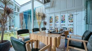 Un comedor con mesa y sillas de madera, un separador de vidrio y vistas al exterior.