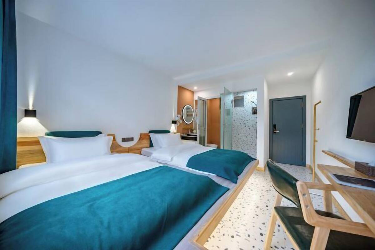 A hotel room with two beds, a desk, a chair, a TV, and a bathroom visible through an open door.