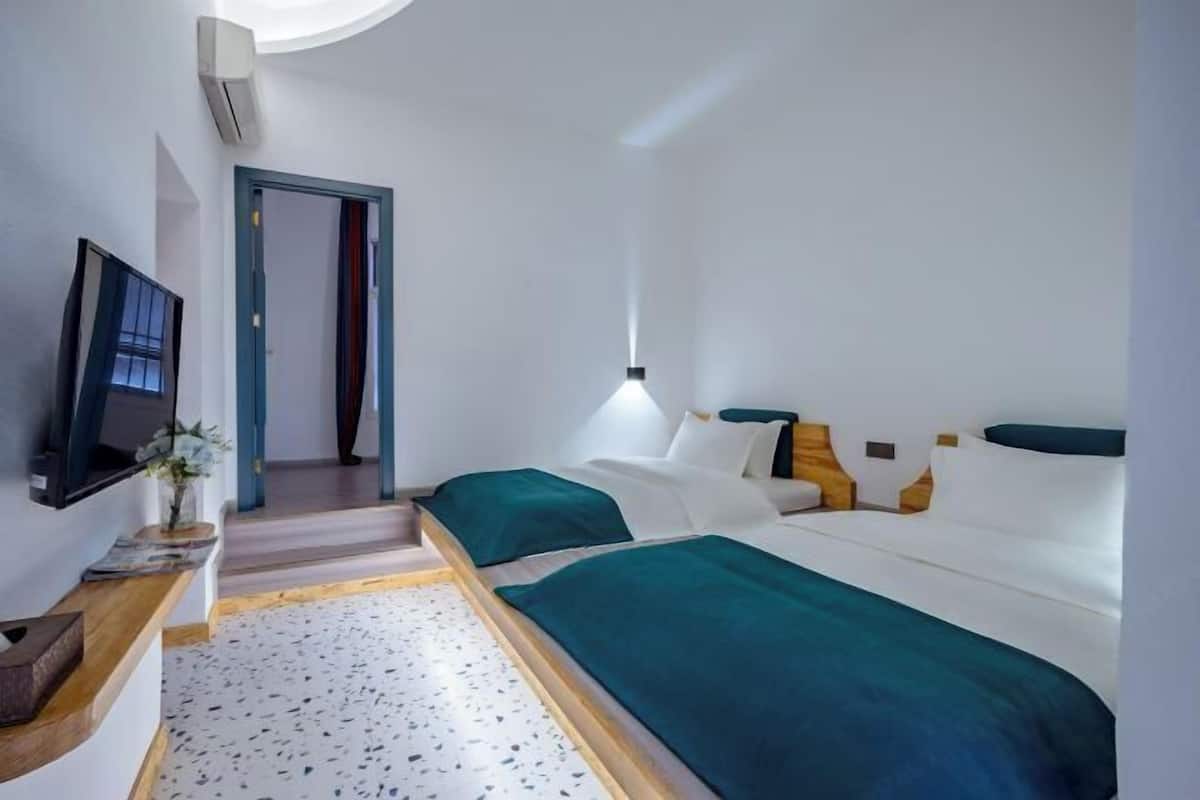 A hotel room with a bed, a TV, a desk, and a door leading to another room.