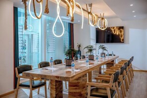 Un salón de conferencias con una larga mesa de madera, sillas y una lámpara moderna.