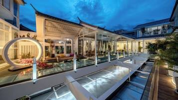 A modern outdoor pool area with a seating area, lounge chairs, and a well-lit walkway.