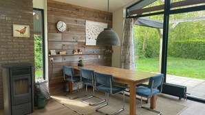 Une cuisine moderne avec une table en bois, des chaises bleues, une cuisinière encastrée et une grande fenêtre donnant sur un paysage verdoyant.