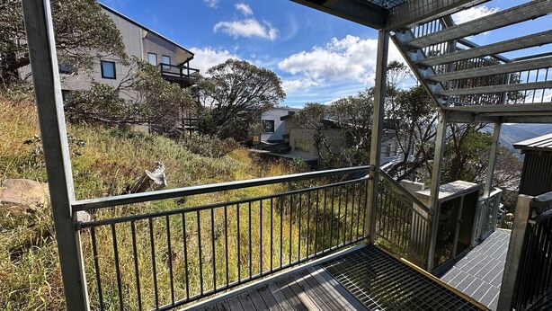 Un balcone con ringhiera metallica che si affaccia su una zona verde con alberi e un edificio sullo sfondo.