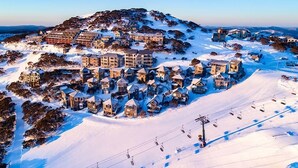 Una stazione sciistica innevata con diversi edifici, tra cui un grande albergo e chalet più piccoli, e una seggiovia in funzione.
