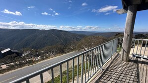 Un balcón con barandilla de metal que da a una carretera y un paisaje montañoso.