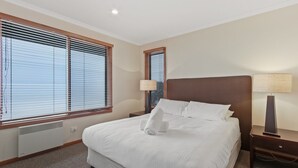 Una habitación de hotel con una cama grande, dos mesitas de noche y dos ventanas con persianas.