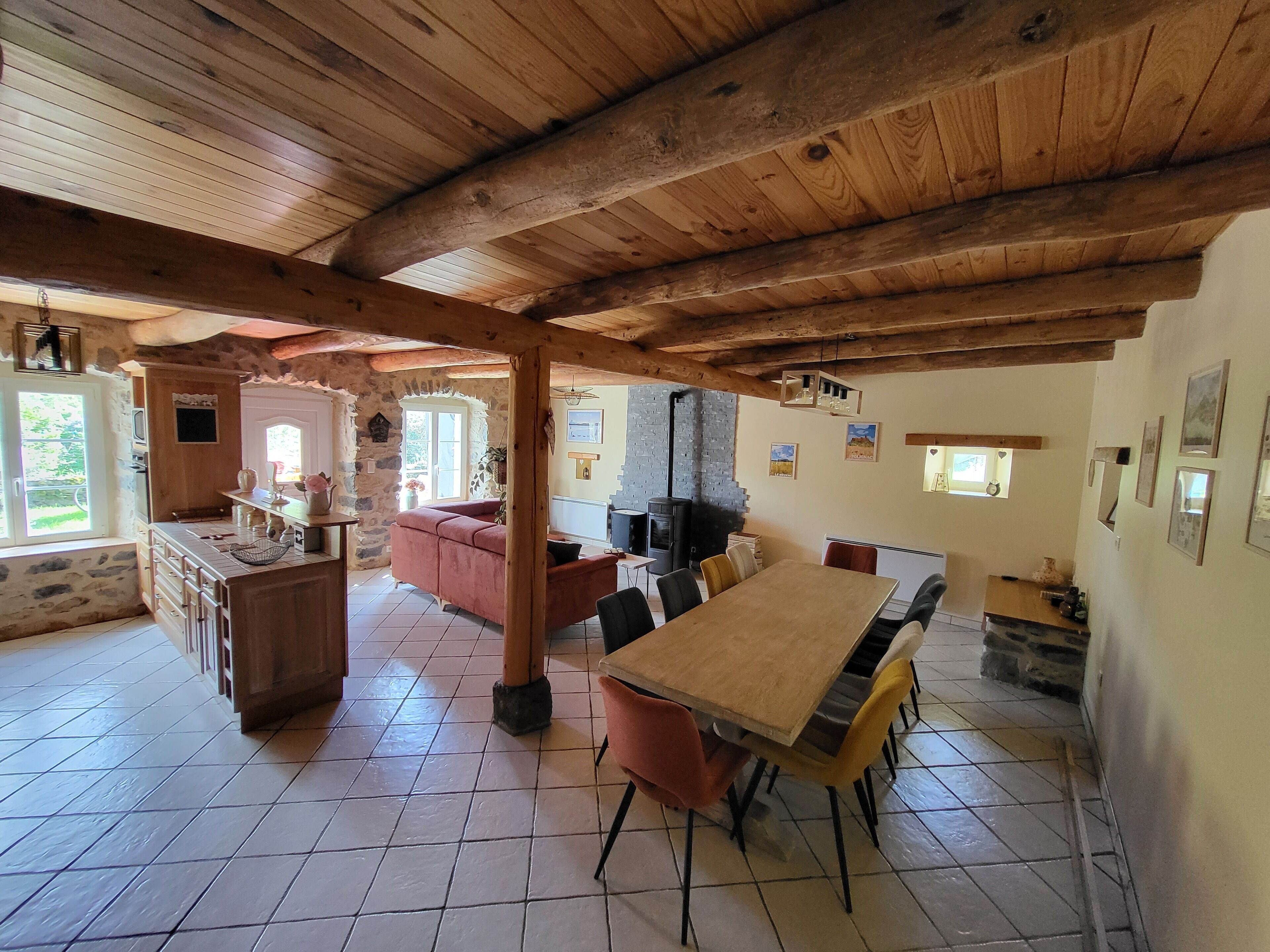 Een rustieke keuken met een houten plafond, stenen muren, een grote eettafel en een inbouwfornuis.