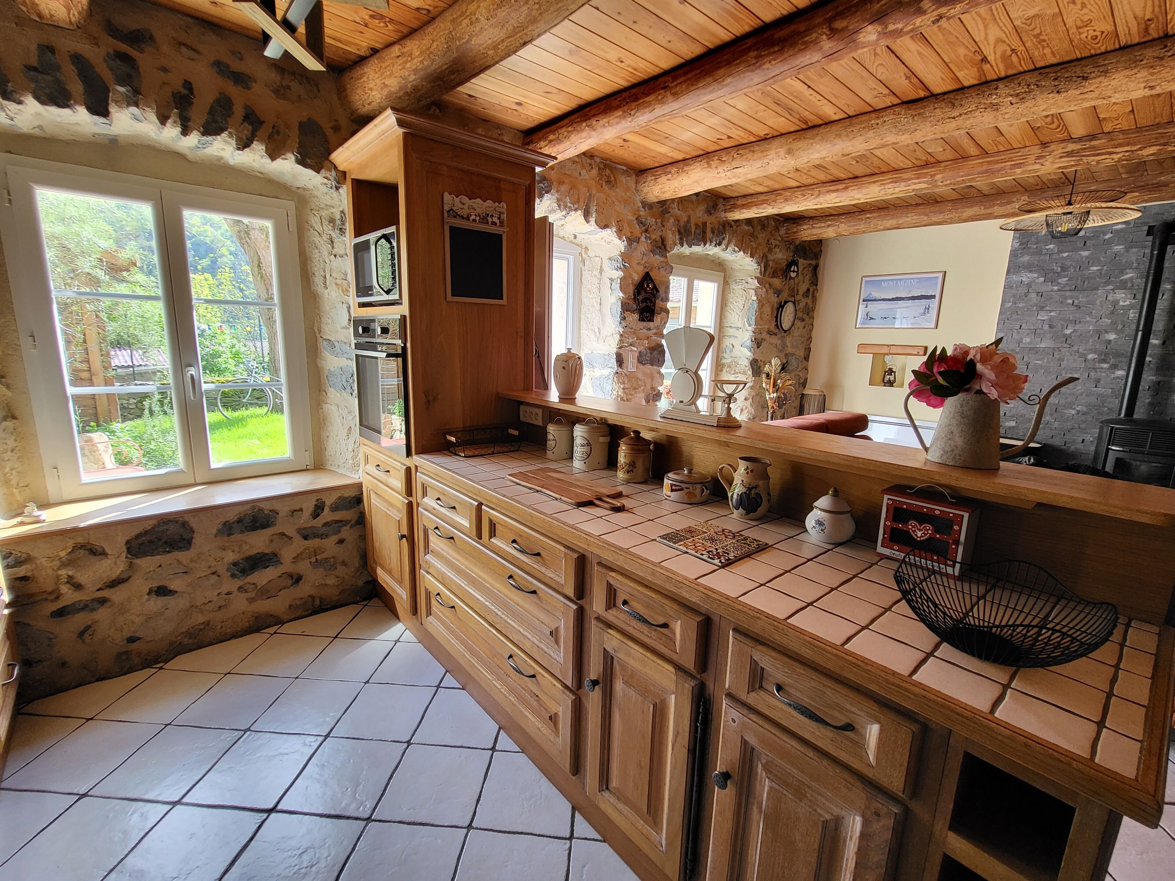 Une cuisine rustique avec des murs en pierre, des armoires en bois et un sol carrelé.