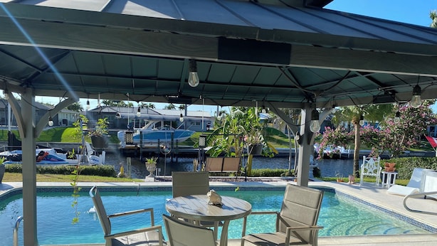 Ein überdachter Außenbereich mit Pool, Liegestühlen und Blick auf einen Yachthafen mit Booten.