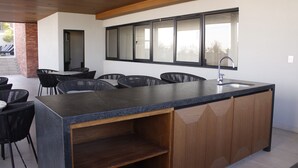Une cuisine moderne dotée d’un grand îlot central, de meubles de rangement en bois intégrés et d’une fenêtre donnant sur l’espace extérieur aménagé pour se détendre.