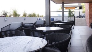 Un espace extérieur aménagé en terrasse, avec des meubles en osier et des tables en marbre, offrant une vue sur un bâtiment et sur quelques éléments de végétation en arrière-plan.
