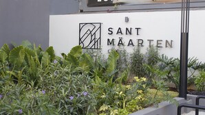 Une enseigne indiquant « SANT MÅARTEN », avec un logo et du texte, entourée d’une végétation luxuriante et d’une rambarde en métal.