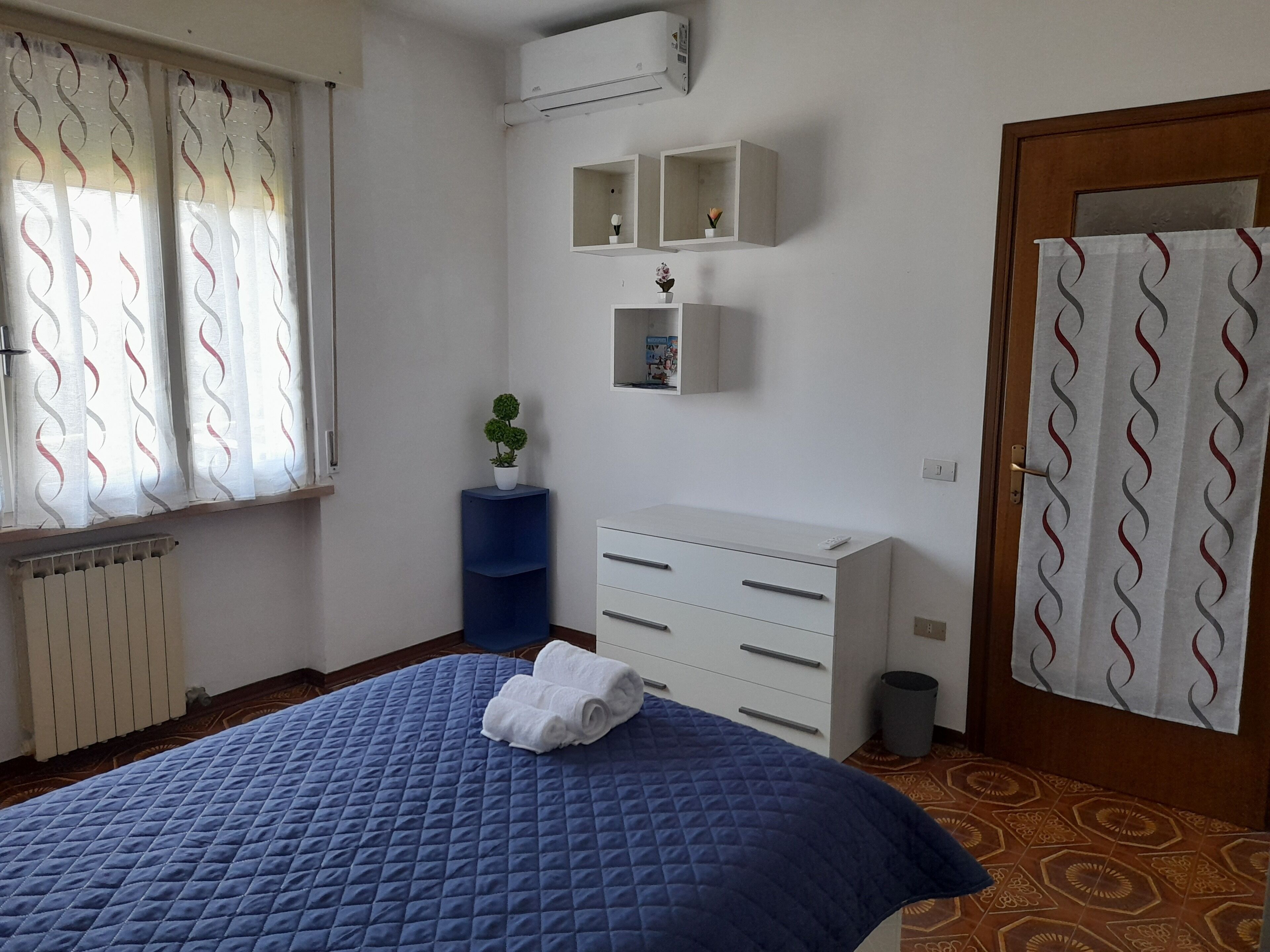 Une chambre à coucher avec un lit, une commode, un radiateur, une plante en pot et un rideau de douche.