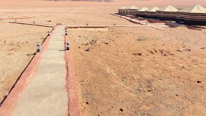 A desert landscape with a paved walkway leading to a row of tents.