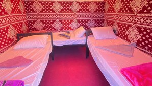 A room with two beds, patterned walls, and a window with sheer curtains.